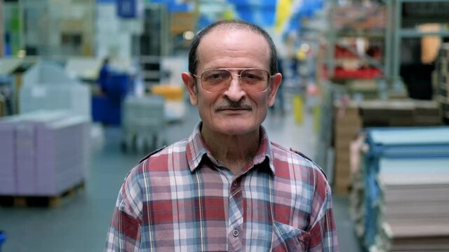 An elderly man in glasses and a plaid shirt in a hardware store looks at the camera. Portrait on a blurred background. The camera moves around