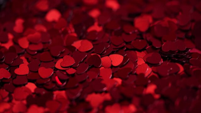 Concept video background for Valentine's Day.Many red shiny heart shaped confetti falling on the table.Close-up video of falling sparkling hearts. 4K