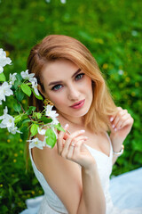 A beautiful young red-haired woman enjoys life in a spring blooming garden with a background of flowering trees. Dreamy pensive young woman on the nature at sunset. Close-up portrait