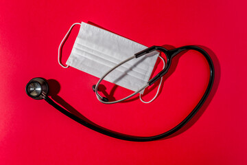 Stethoscope and surgical mask on red background