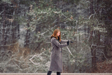 A young girl in a gray coat is keen on photography. Taking pictures of the winter forest and beautiful scenery on the phone.