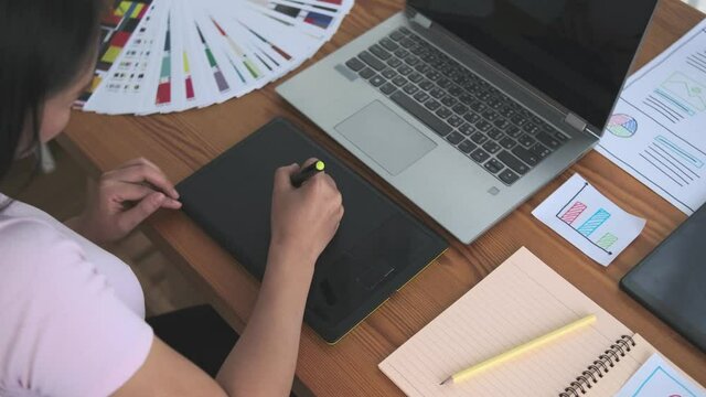 Creative designer graphic web developer UI UX worker employee Working at home, Asian woman using digital graphics tablet sketching drawing workspace desk slow motion side view happy smiling freelance.