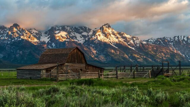 Beautiful golden sunrise timelapse at a farm with barn and snow capped mountain, clouds flowing by at the T.A. Moulton Barn, Grand Teton National Park, Wyoming United States