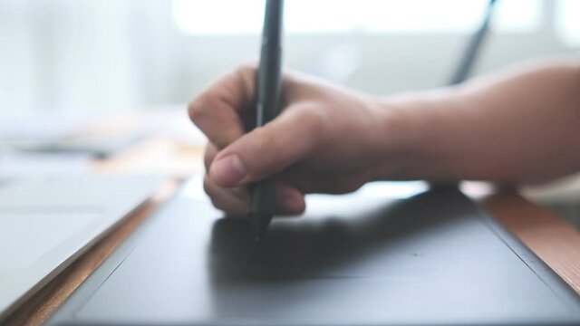 Creative designer Asian woman close up hand using stylus drawing sketching UI UX ideas project design on notebook and laptop, computer slow motion busy working at home modern office desk workspace.