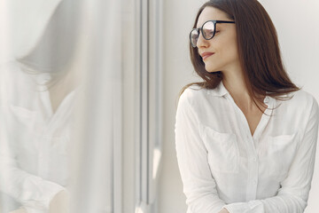 Girl in a office. Woman in a white shirt. Lady in a glasses standing by the window.