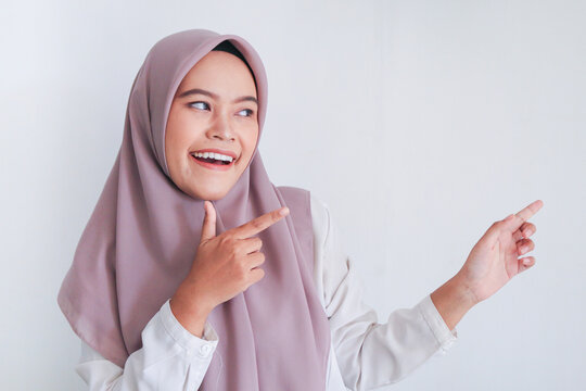 Asian Islam Muslim woman wearing headscarf is pointing finger to blank copy space smile face area. Indonesian woman. Religion concept isolated on gray background