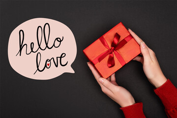 Cropped view of woman holding red gift near speech bubble with hello love lettering on black