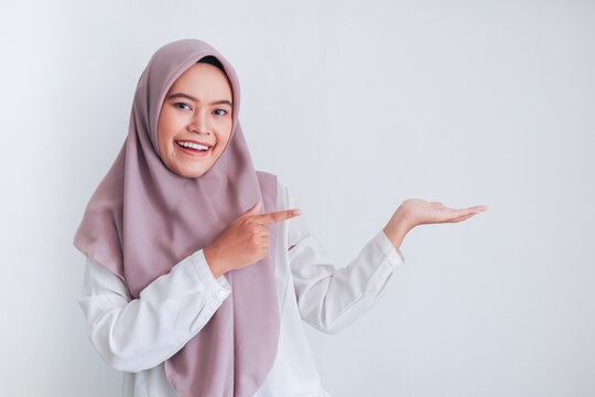 Asian Islam Muslim woman wearing headscarf is pointing finger to blank copy space smile face area. Indonesian woman. Religion concept isolated on gray background