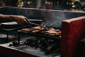 Roasting meat on a grill, hand with tongs turning the meat.
