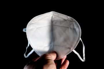 Holding a white new FFP2 mask in the hand and looking on it. Certified disposable protection to reduce aerosol emission during Covid-19 pandemic on a clean black background.
