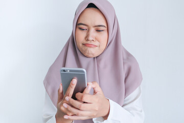 Young Asian Islam woman wearing headscarf is sad and cry in what she see on the smartphone. Indonesian woman on gray background