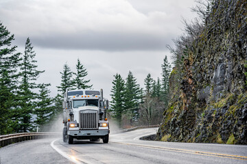 Fototapeta na wymiar White industrial big rig semi truck with semi trailer turning on the winding mountain road at rain