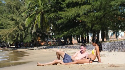 Interracial pregnant young couple lying on the sand in the beach on a sunny day. - Powered by Adobe