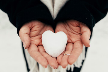Obraz premium Snow heart snowball in girl gloved hands. Blurred background