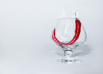 Smoke chili pepper in a glass on a light background