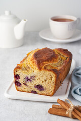 Banana bread, sliced cake with banana and blueberries. Morning breakfast with tea on light gray cincrete background, vertical