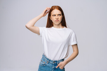 Astonished confused young woman wearing T-shirt and denim pants touching head with hand on isolated...
