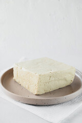 tofu cheese is large piece on plate on white background. Healthy dietary vegetarian food, vertical food content, selective focus