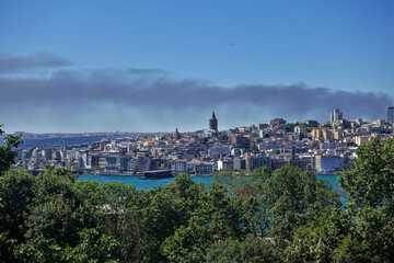 Panorama of Istanbul from above. In the foreground are tree branches and the Bosphorus. In the distance is an urban area with modern and old buildings. Blue sky, summer day.Turkey