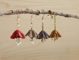 flower shaped leather earrings hanging on tree branch on wood background