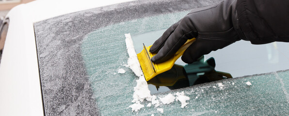 Hand in glove scraping ice or snow from car windscreen, winter problems in transportation concept
