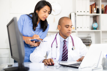 Two focused doctors working with patient records on laptop in modern medical office