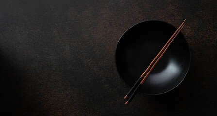 empty black ceramic bowl with chopsticks on dark brown stone background, top view, copy space