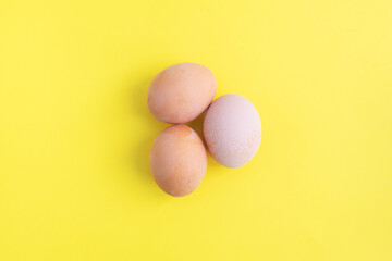 Three brown chicken eggs on a yellow background. Top view, copy space.