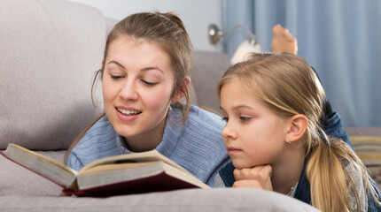 Mother and her daughter spending time at home and reading book together