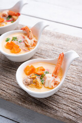 Homemade style steamed egg with shrimp and vegetables in a ceramic bowl on wooden table. healthy food concept.