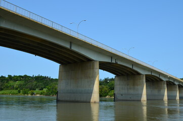 A long and wide cement manmade bridge that hovers over a beautiful river scenery, connecting each...