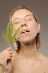 CBD cosmetics concept. Beautiful woman with a cannabis leaf on gray background