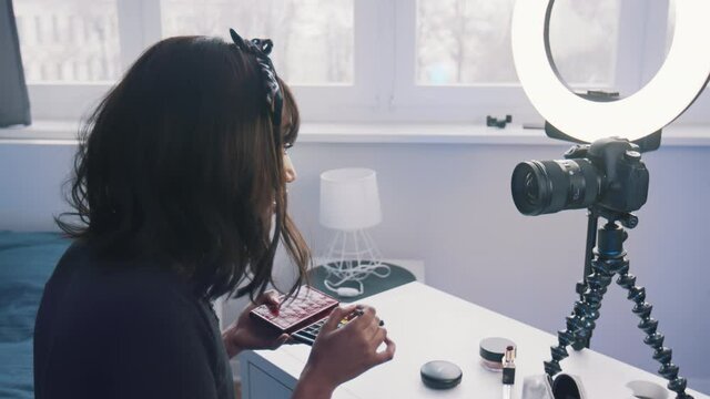 Young woman with black hair applying make up in front of the camera. High quality 4k footage