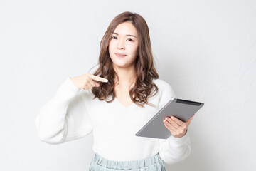 Fototapeta premium 白い壁の前に立って、タブレットを使う若い女性