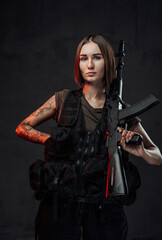 Holding assault rifle martial woman in black armour with short haircut poses in dark background.