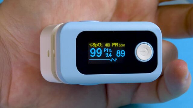 Unrecognizable male person monitoring SpO2 oxygen saturation. Pulse oximeter probe applied to human's finger on blue background. Healthcare and medicine concept. Medical service and check patient