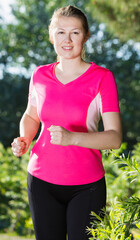 Athletic female in pink T-shirt is running around in the park.