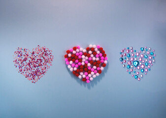 Valentine's day concept. Sparkling pink confetti soft pom poms and rhinestones in shape of heart on blue background. Flat lay style