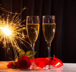 Champagne glasses on a dark background, a red rose and a sparkler. The concept of Valentine's day.