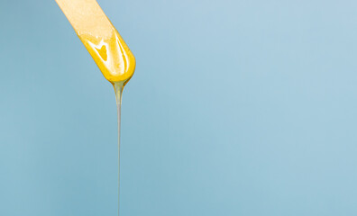 Sugar depilatory paste drips from a wooden spatula. The removal of body hair. Free space for text, blue background.
