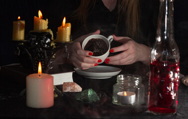 Fortune-telling on coffee grounds. A fortune teller's hands, a Cup of coffee, candles, and skulls on a black table. The concept of wizards, witchcraft and magic.