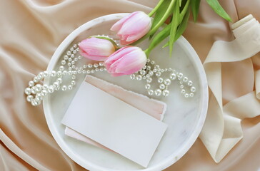 blank greeting card, invitation mock up and pink tulip flowers on marble tray top view. wedding, birthday, mother's day, Holiday background.Stationery still life with blank paper sheets.copy space