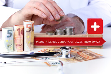 Medizinisches Versorgungszentrum (MVZ). Arzt stapelt Geld Münzen auf einen Geldstapel. Text mit...