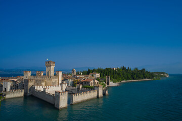 Obraz premium Amazing view to the old bridge and harbor of Sirmione. Aerial view on Sirmione sul Garda. Italy, Lombardy. View by Drone. Rocca Scaligera Castle in Sirmione.