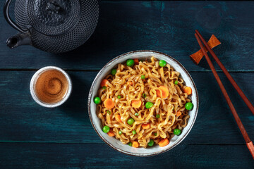 Noodles with vegetables and tea, top flat lay shot on a dark blue wooden background