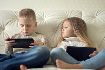 Two little children boy and girl holding tablet and watching cartoons at home, having fun with digital device.