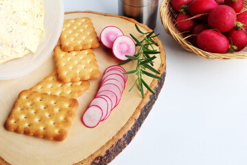Crispbread with butter and sliced radish on wooden cutting board.