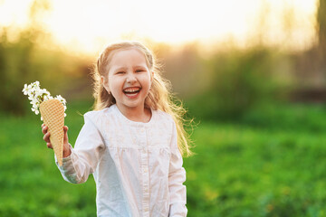 little girl is laughing and holding tree's spring flowers in waffle cone