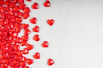 Small red heart shape transparent candies or glass decorations laying on white wooden background at left side as a lovely greeting backdrop on saint valentine's day. Image with copy space, horizontal