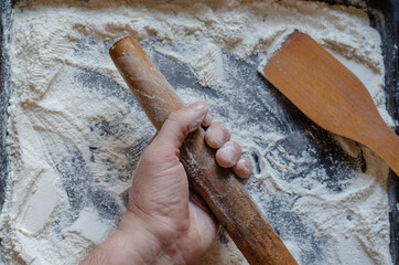 Hand, wooden rolling pin, spatula and wheat flour.